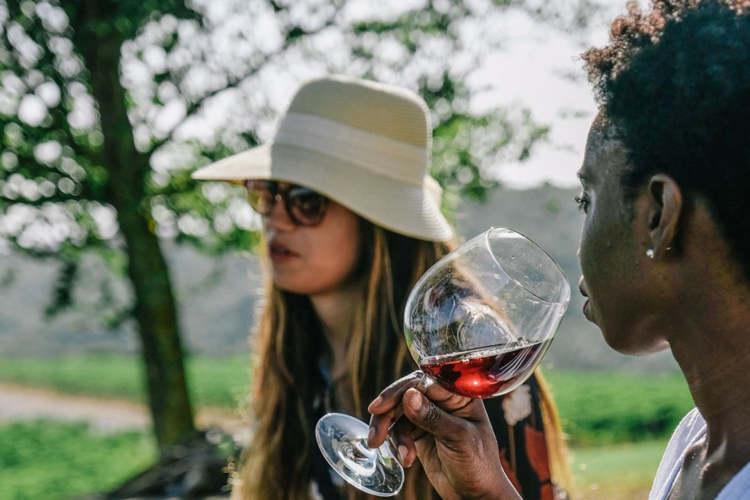 Two women outdoors during a Tuscan wine tour, one holding a glass of red wine.